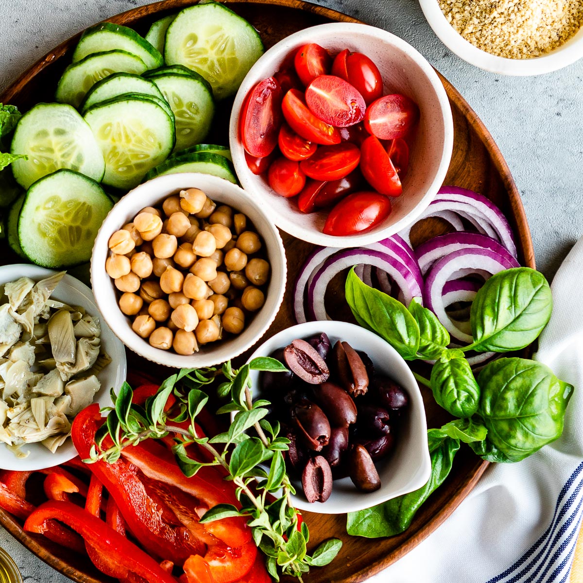 wooden circle tray full of white bowls with fresh ingredients for vegetarian Mediterranean recipes.