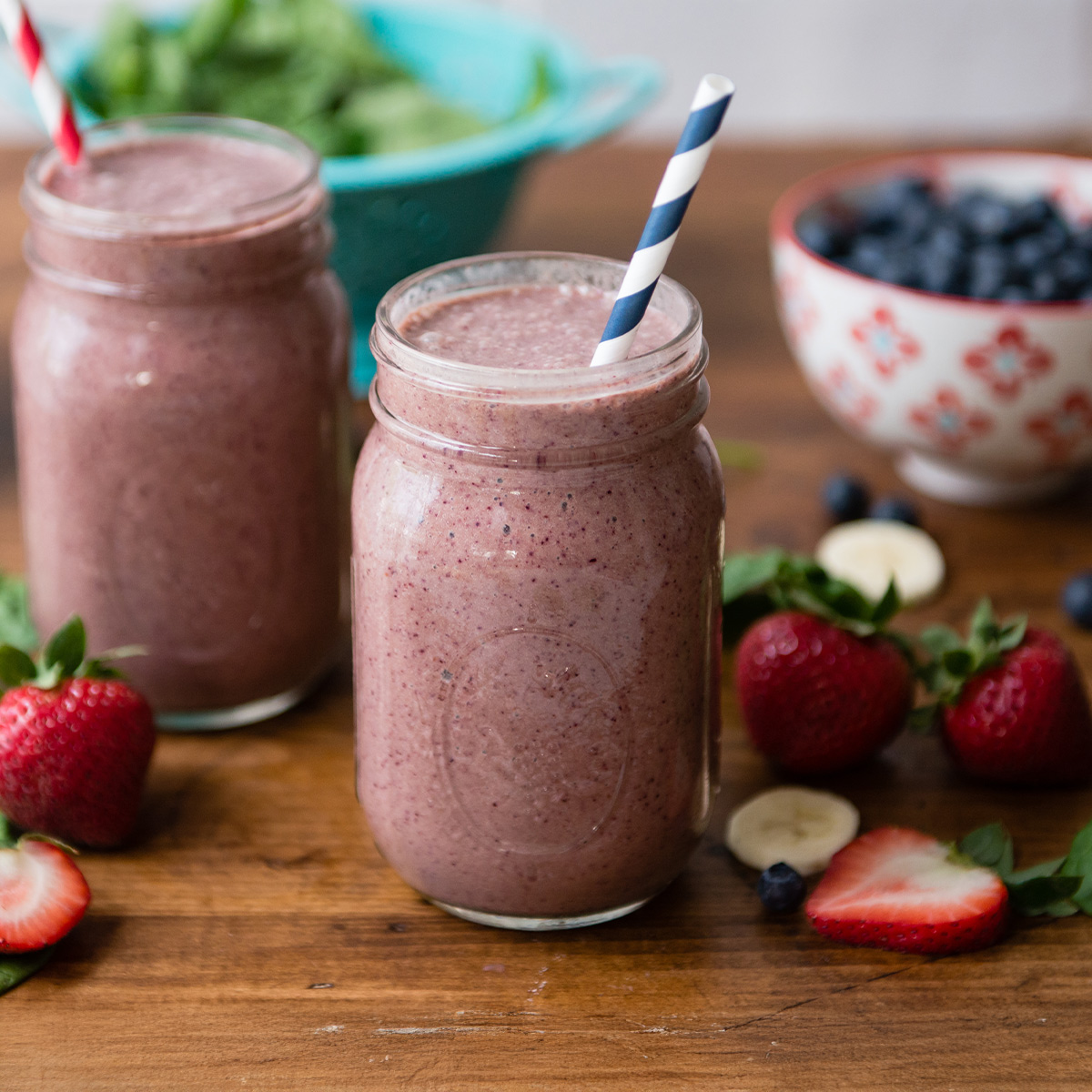 Two berry smoothies surrounded by fresh berries