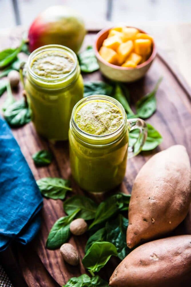 sweet potato smoothie in a glass jar on a cutting board surrounded by whole sweet potatoes and spinach.