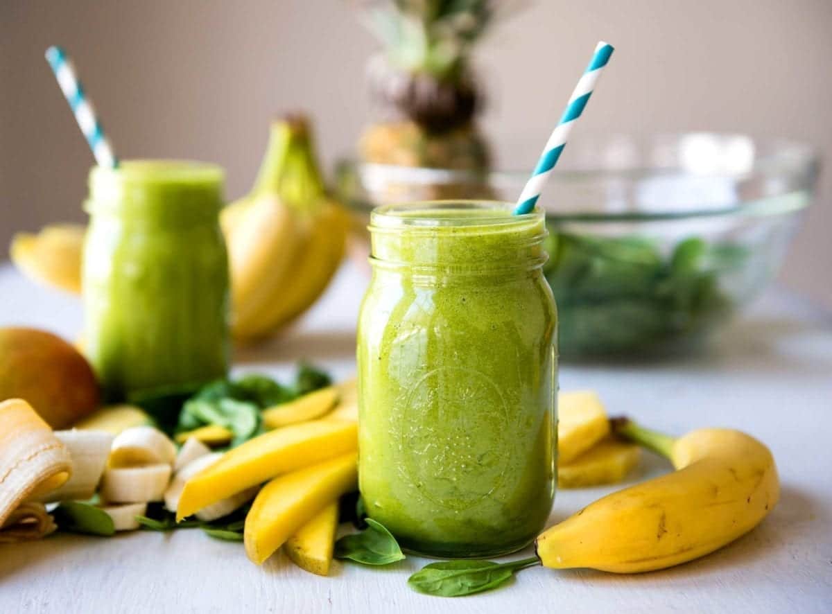 Two mason jars filled with blended green smoothie on countertop.