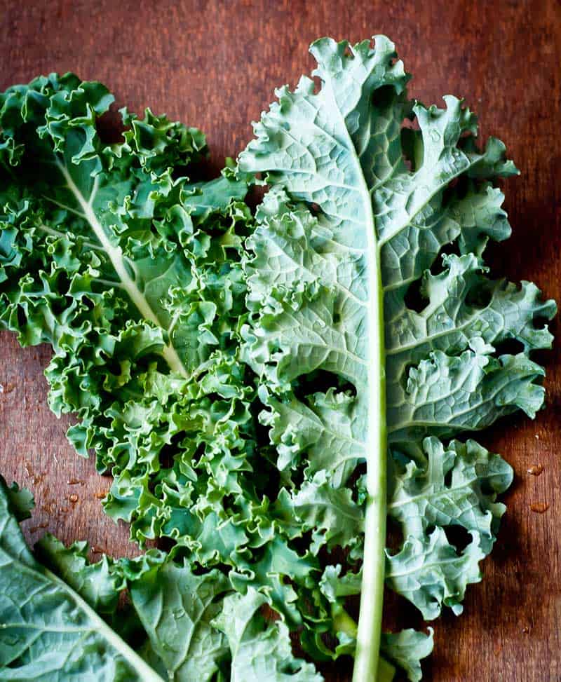 big stalks of curly kale leafy greens on wooden table top
