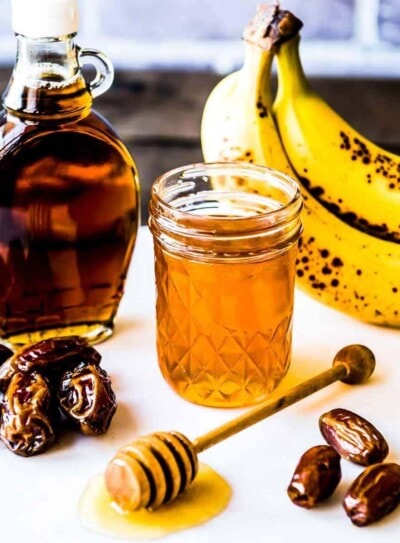 examples of natural sweeteners including bananas, honey in a glass jar, maple syrup and dates.