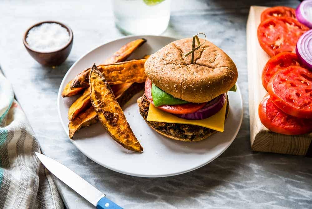 vegan black bean burger loaded with fresh toppings, a gluten free bun, and sweet potato wedges.