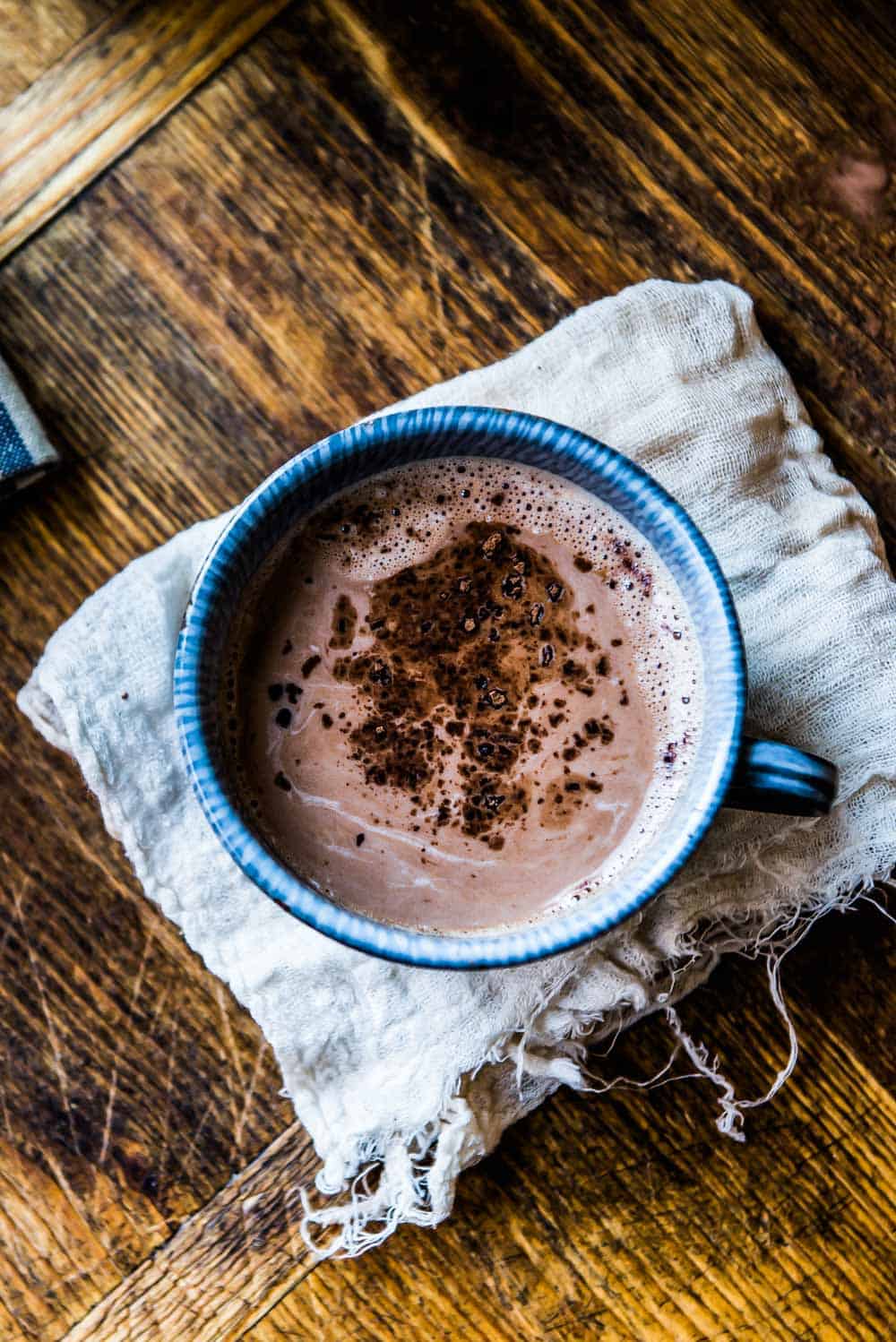 foamy cup of vegan hot chocolate with cacao nibs in a blue mug.