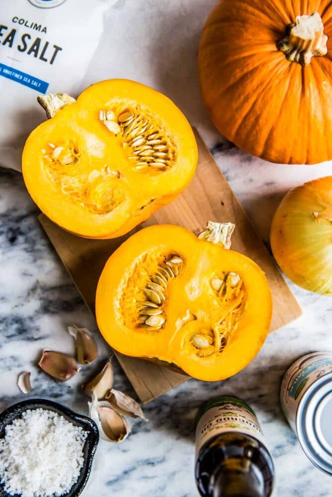 a pie pumpkin cut in half on a wooden cutting board, ready to be roasted for this pumpkin soup recipe.