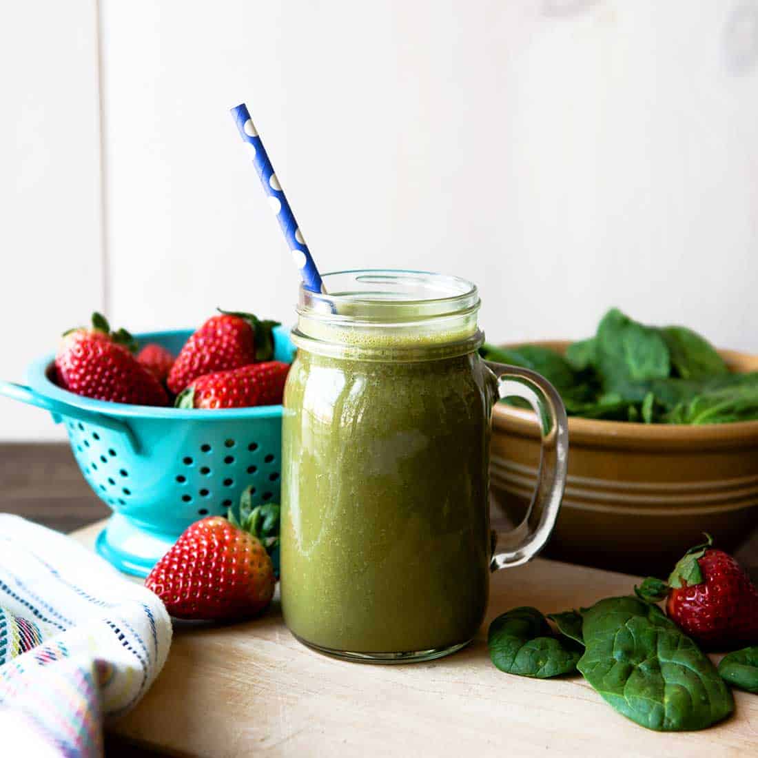 spinach strawberry banana smoothie in a glass mug surrounded by fresh spinach and strawberries
