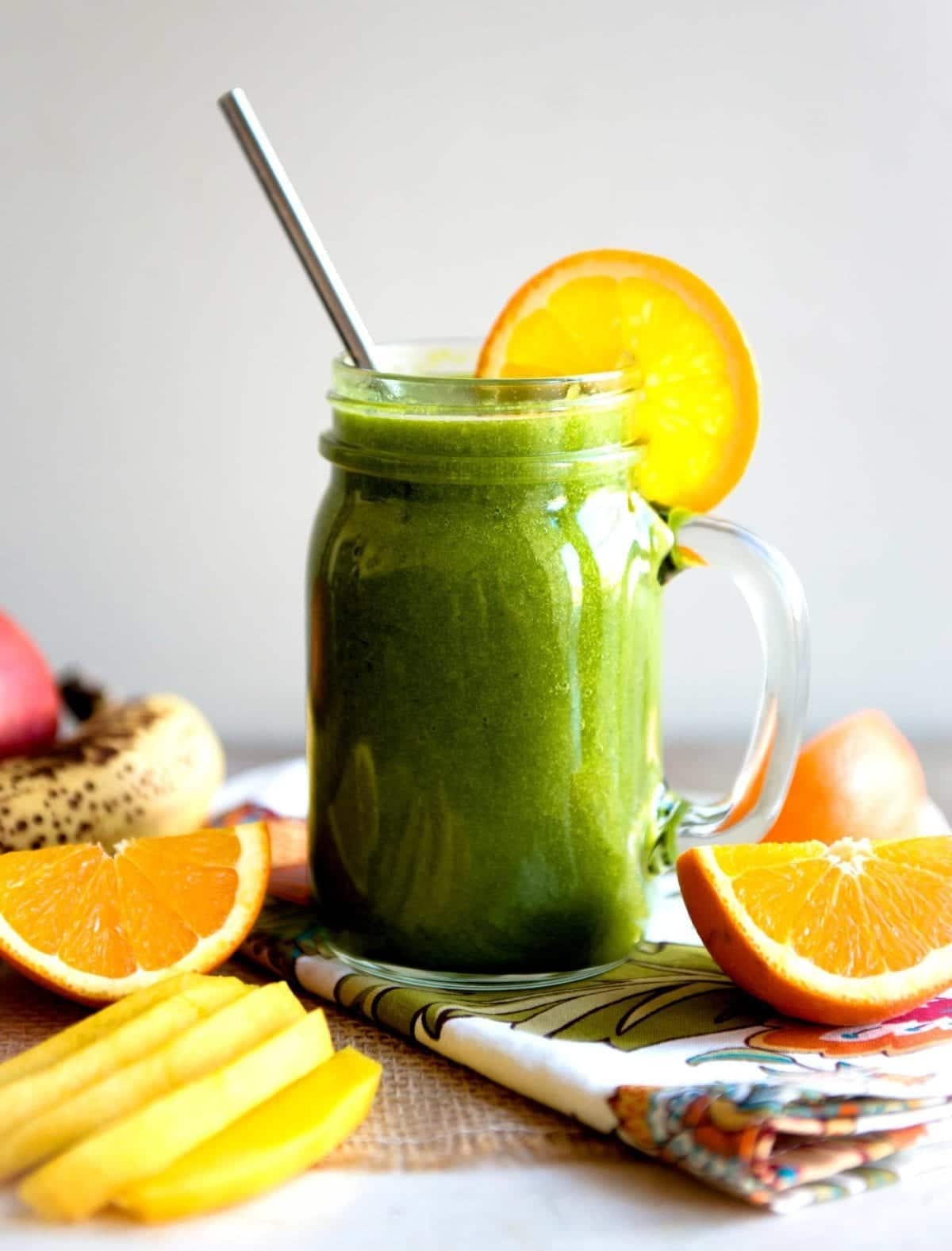 mango orange smoothie in a glass jar with a striped straw and orange slices.