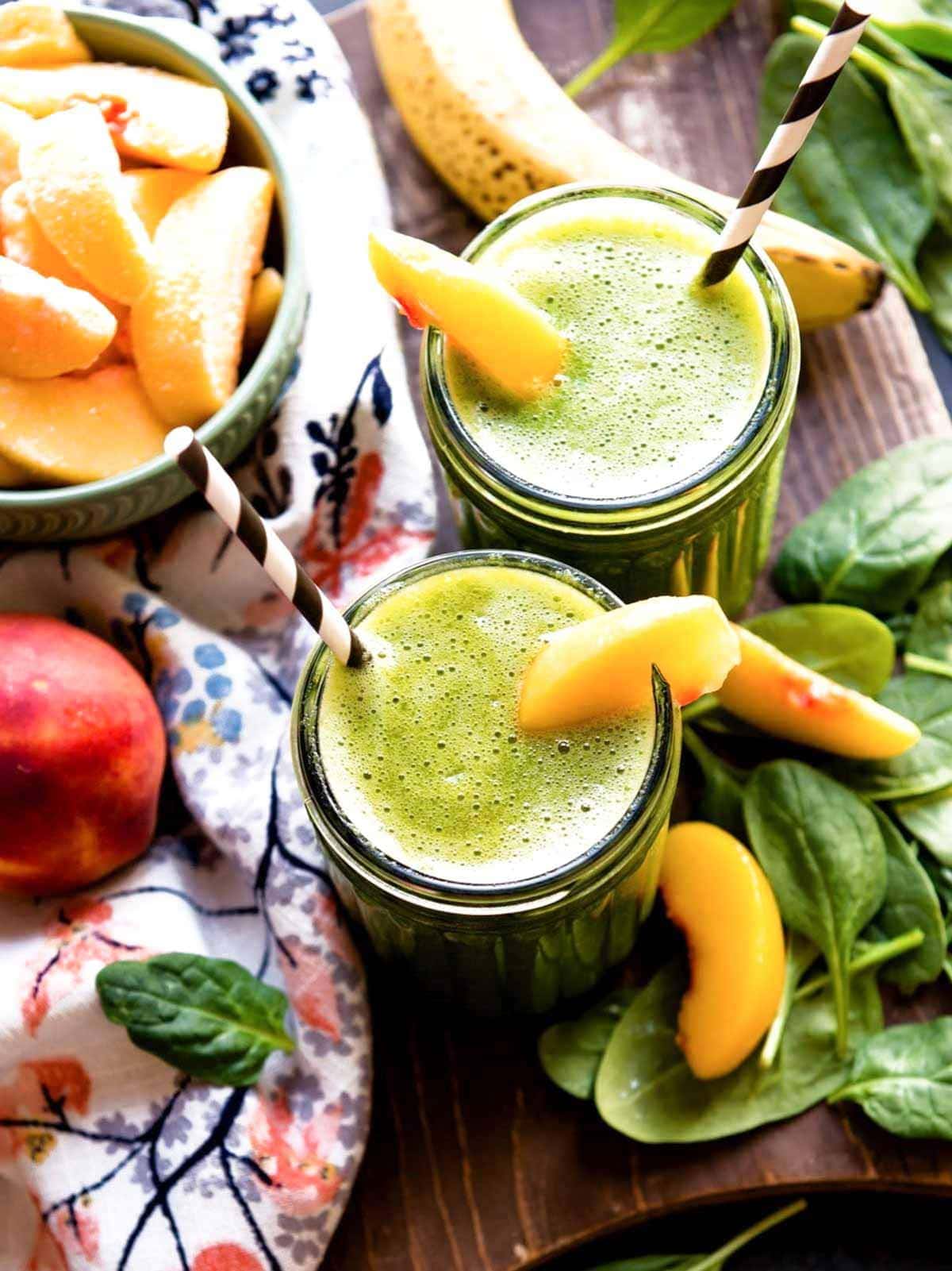 2 glass jars of banana peach smoothie with peach slices and paper straws.