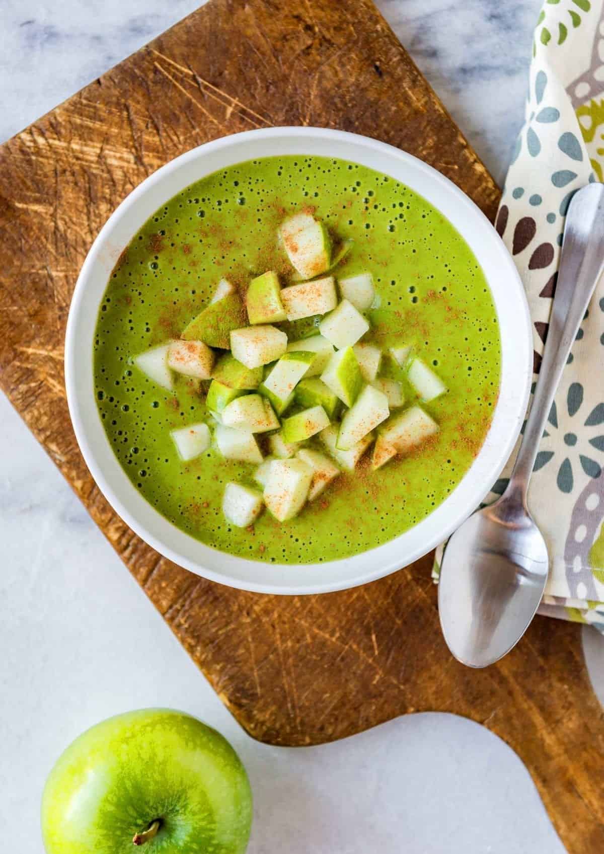 green smoothie in a white bowl topped with cinnamon and chopped green apples.