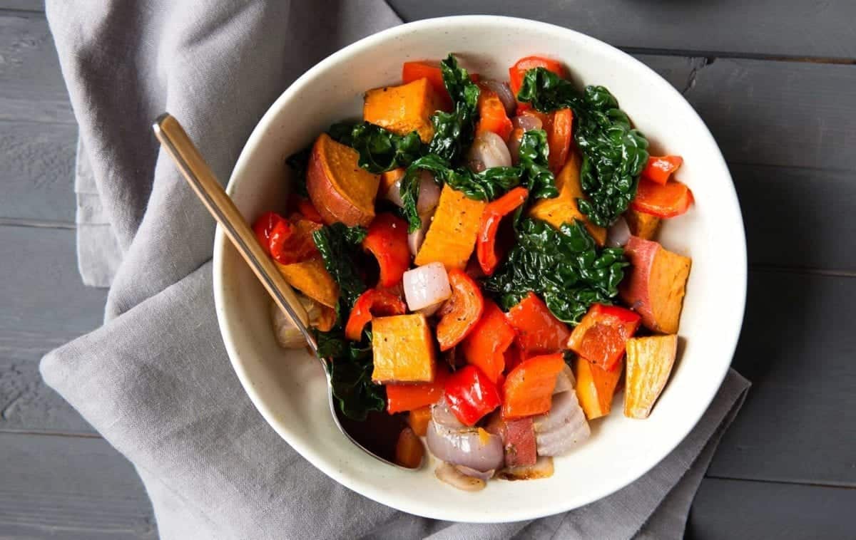 white bowl full of colorful veggies with a spoon and napkin.