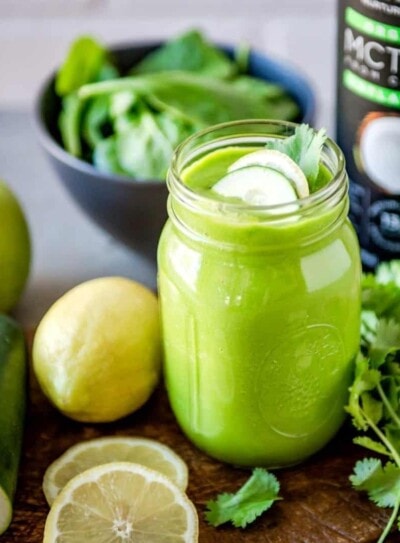 green smoothie in a glass jar next to green ingredients and a bottle of mct oil.