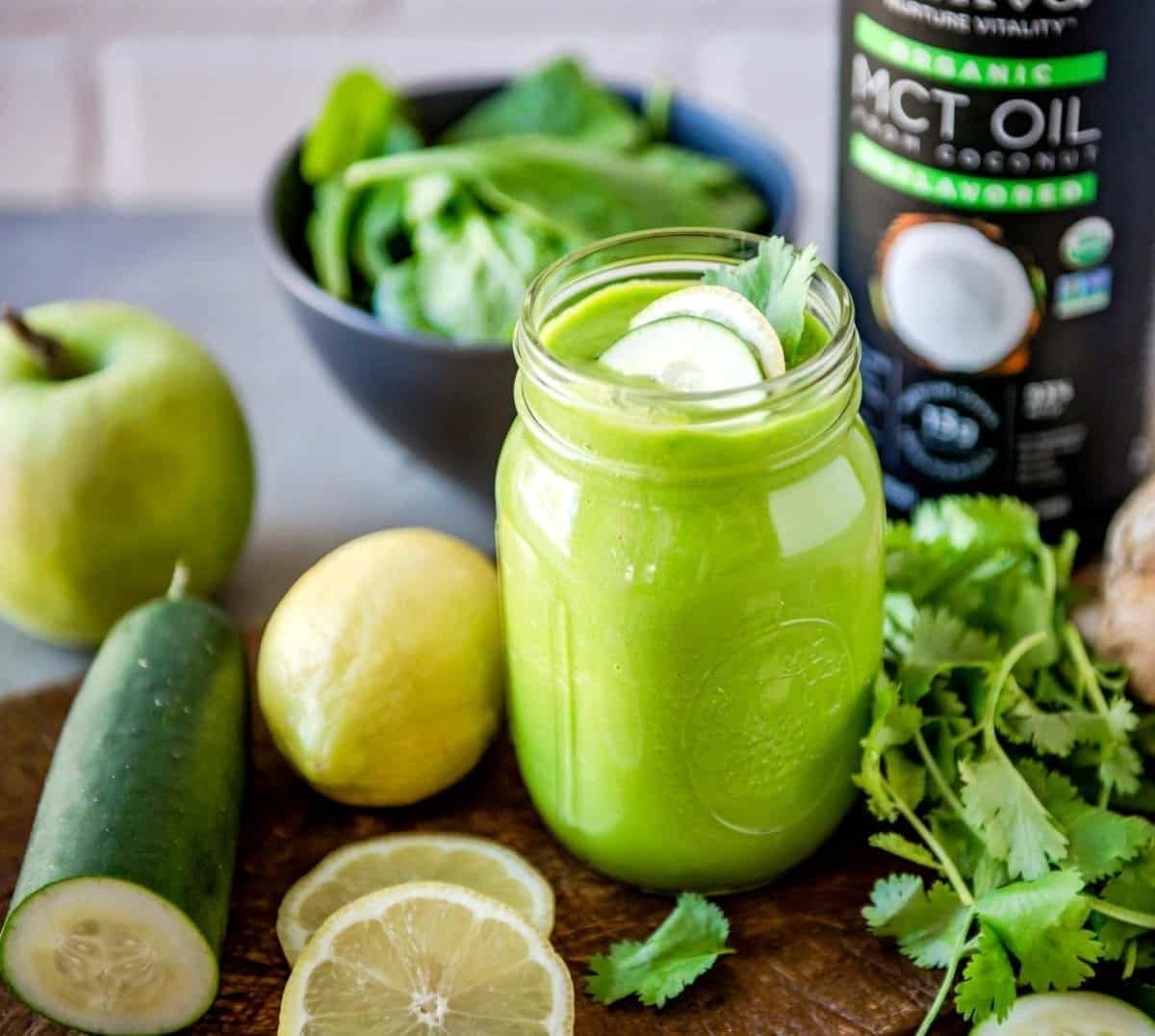 green smoothie in a glass jar next to green ingredients and a bottle of mct oil.
