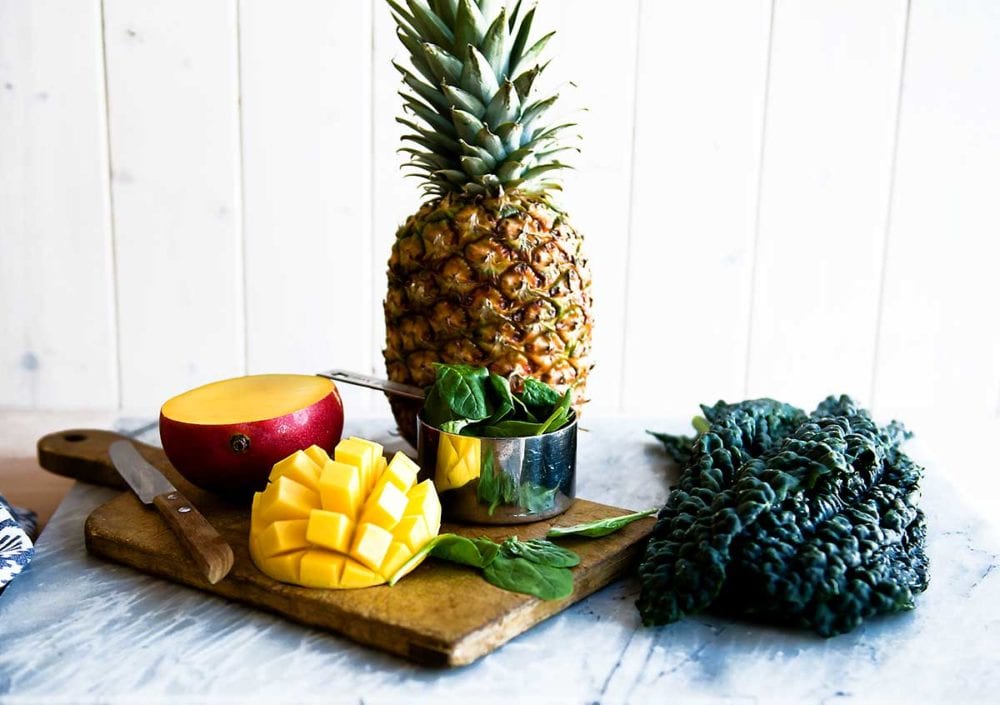 Kale, mango, pineapple and spinach on a cutting board for a smoothie.