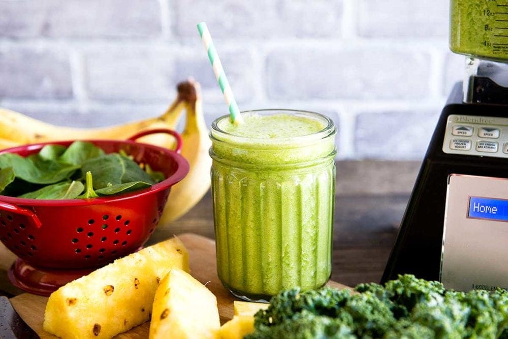 Mason jar with Spinach Kale Smoothie and Blendtec blender in the background.