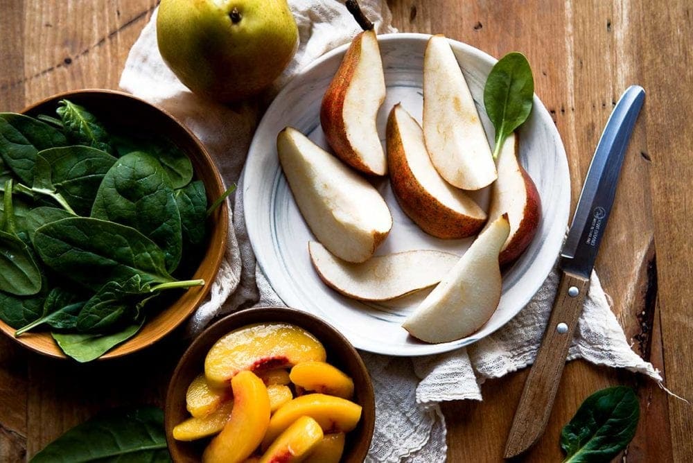 Sliced ripe pears on a plate with a knife and spinach to make a smoothie.