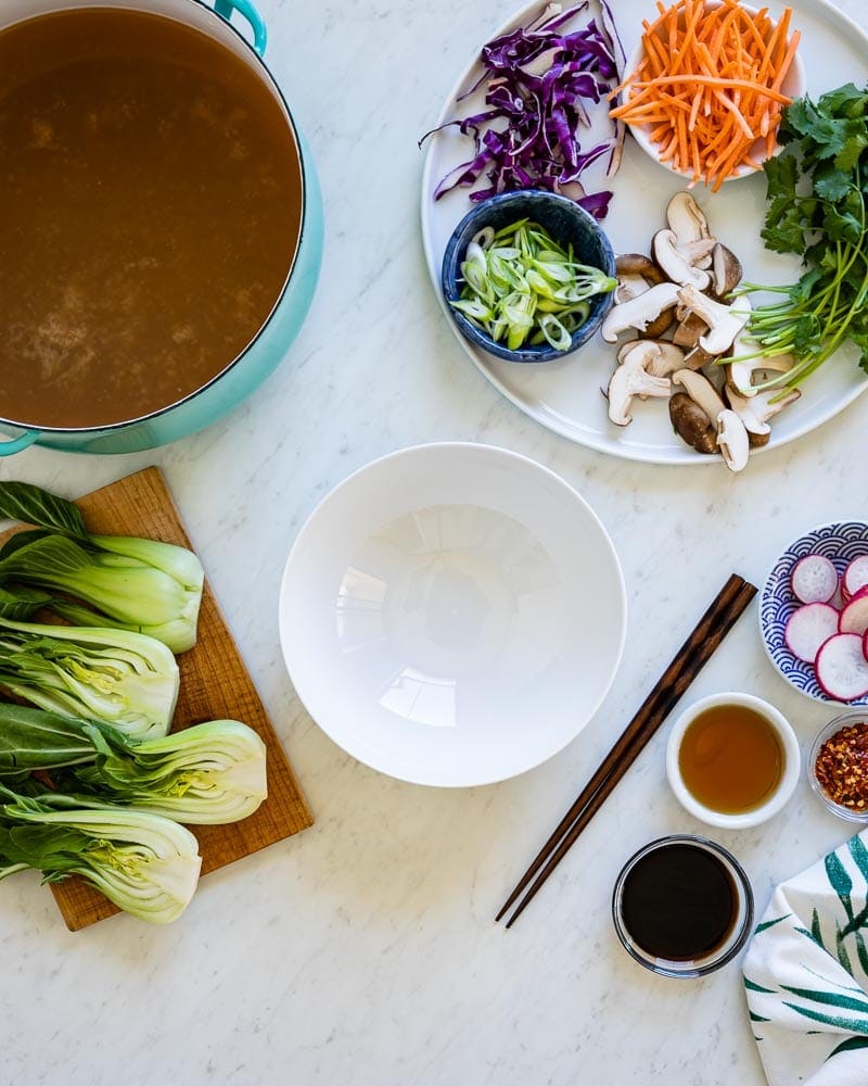 blue stock of vegetable stock next to a white tray of fresh vegetables.