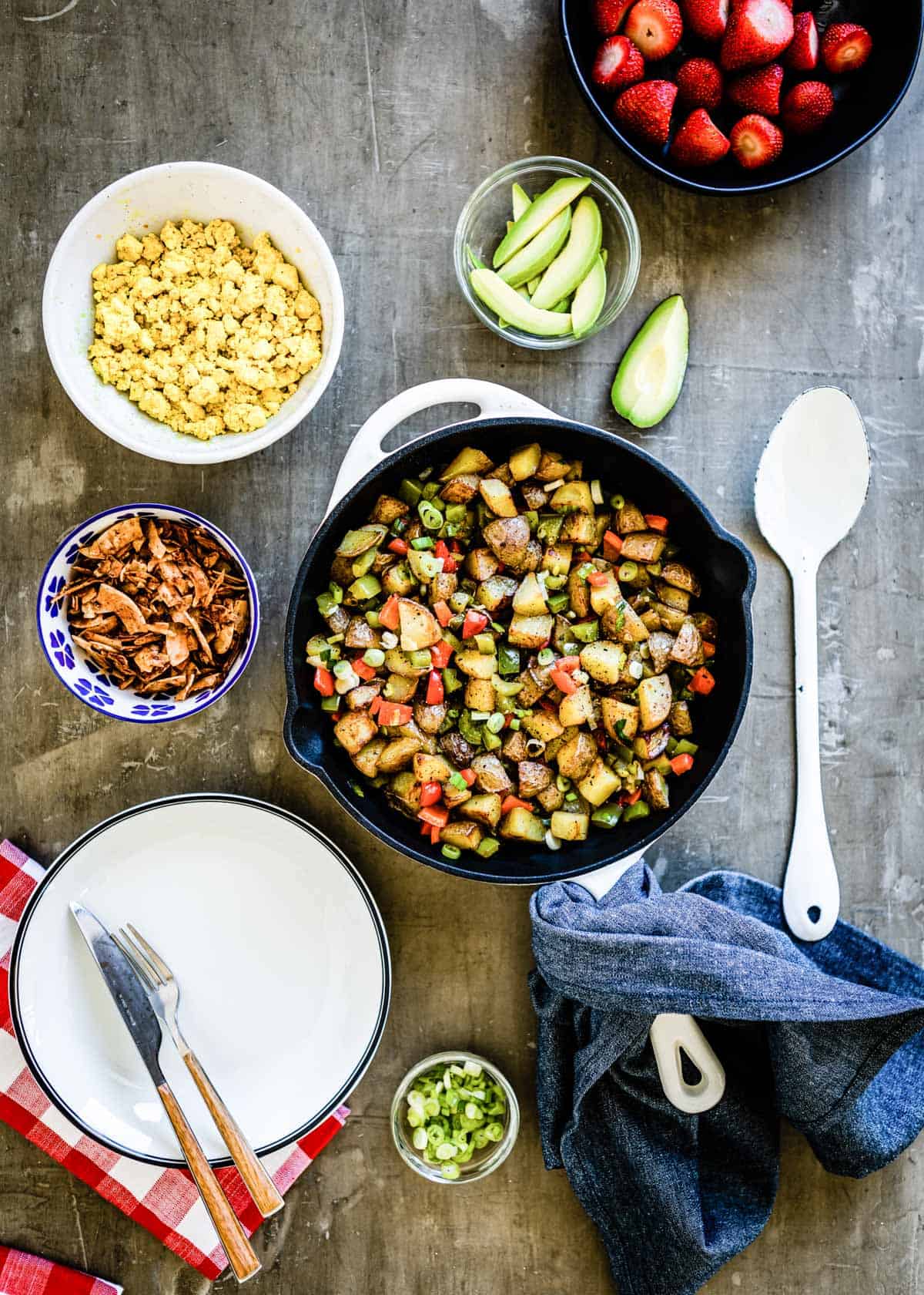 skillet with ingredients for a breakfast bowl recipe, next to a bowl of coconut bacon.