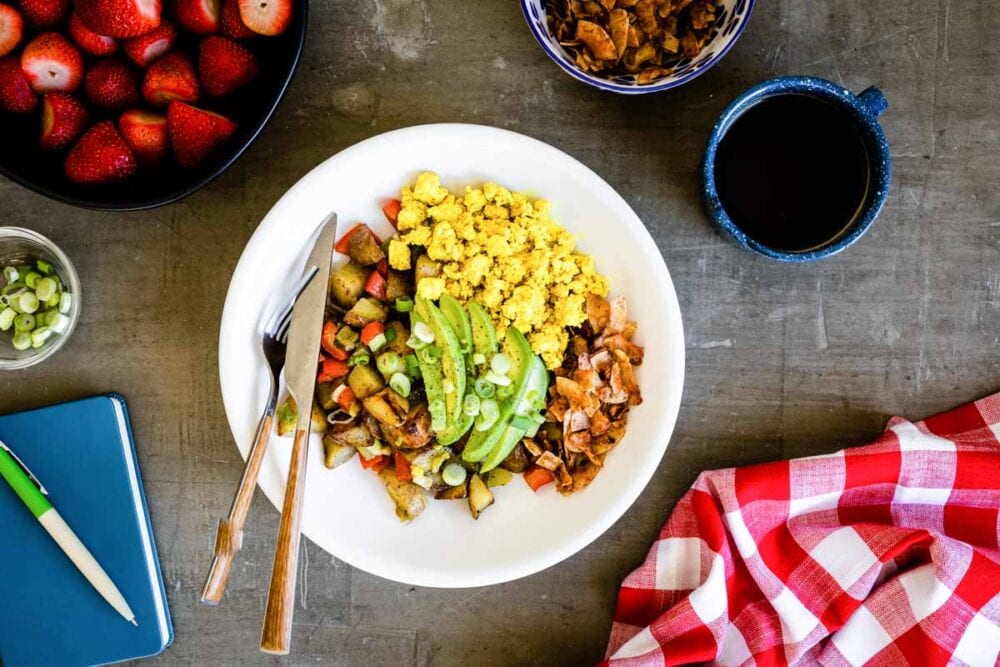 A delicious, vegan breakfast bowl with tofu, coconut bacon, sliced avocados and potatoes.