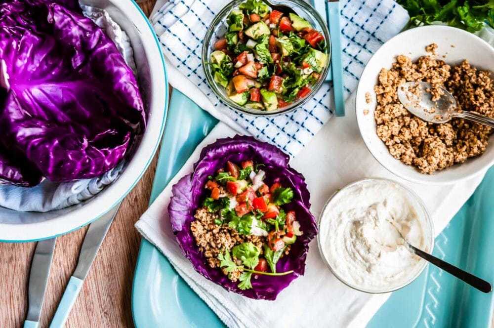 bowls of fresh pico de gallo, walnut taco meat, cashew cream and purple cabbage leaves next to a prepared taco.