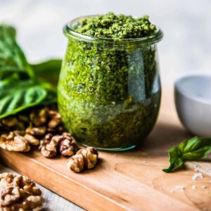 pesto de manjericão vegano em uma jarra de vidro cercado por manjericão e nozes.