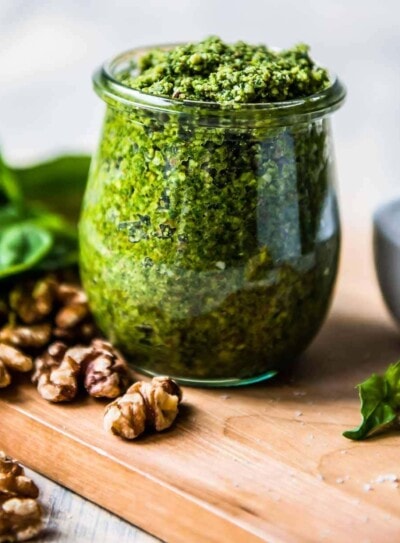 vegan basil pesto in a glass jar surrounded by basil and walnuts.