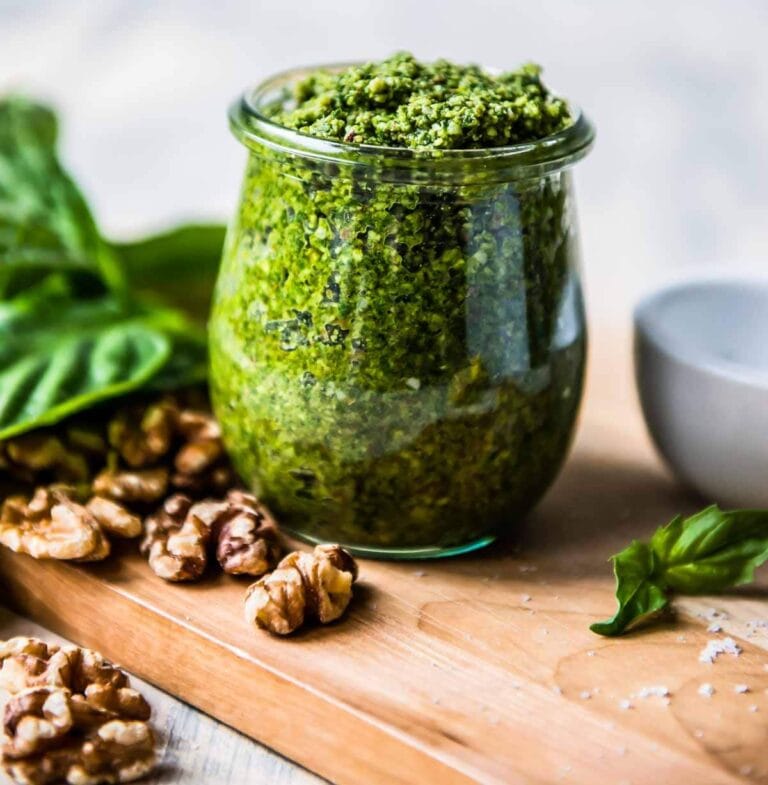 vegan basil pesto in a glass jar surrounded by basil and walnuts.