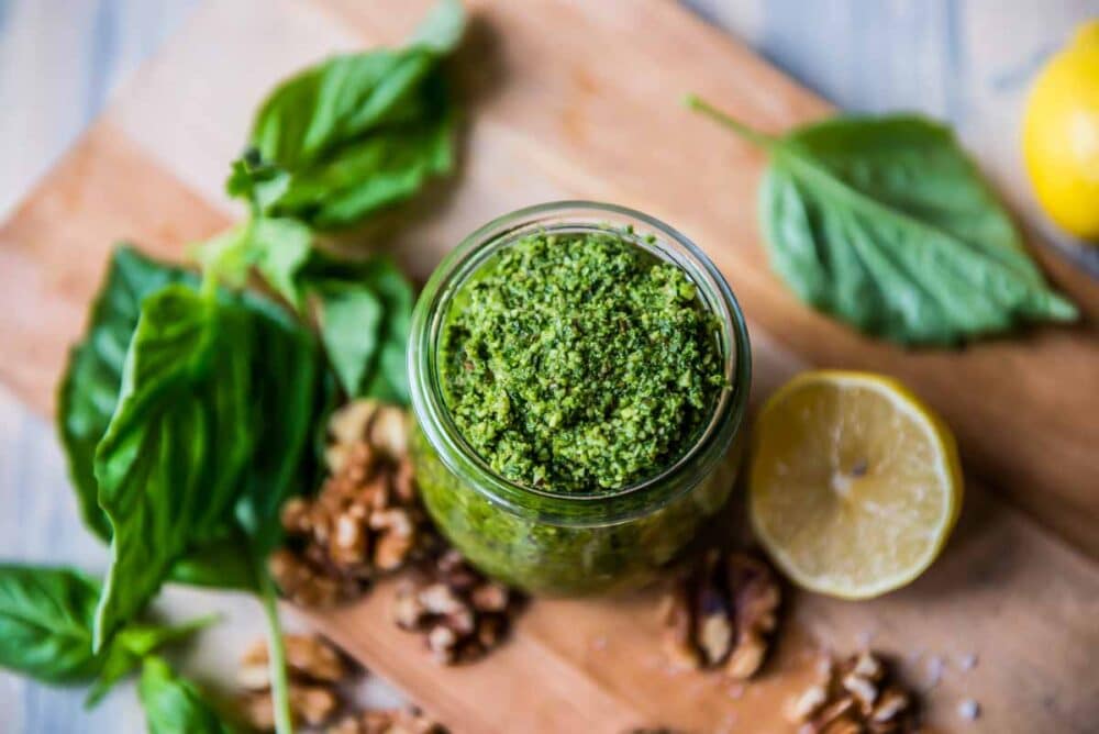 vegan basil pesto in a glass jar on a wooden cutting board.