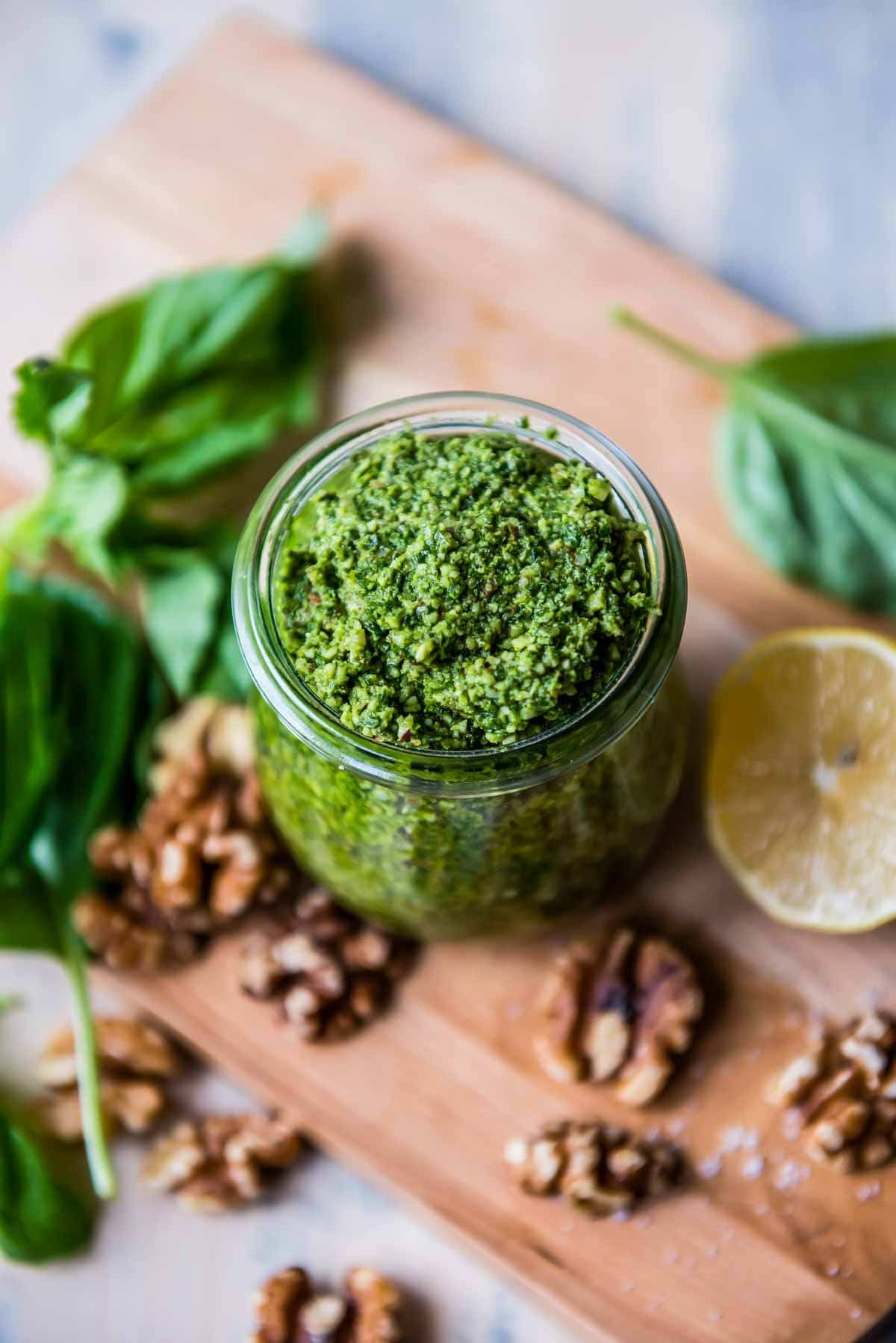 fresh pesto in a glass jar surrounded by fresh ingredients.