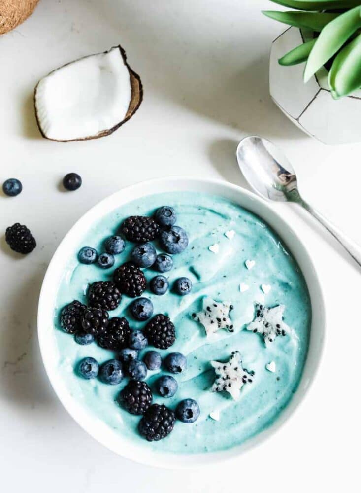 blue ice cream in a white bowl with fresh berries and dragon fruit stars.