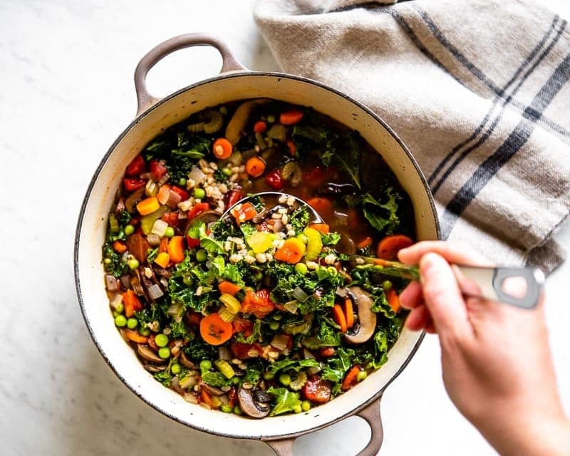 nutrient-dense vegetable barley soup in a stock pot with a soup ladle.