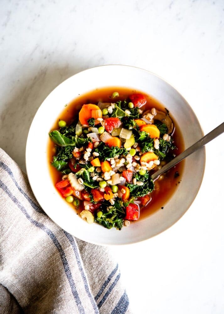 white bowl of barley soup with a stainless steel spoon.