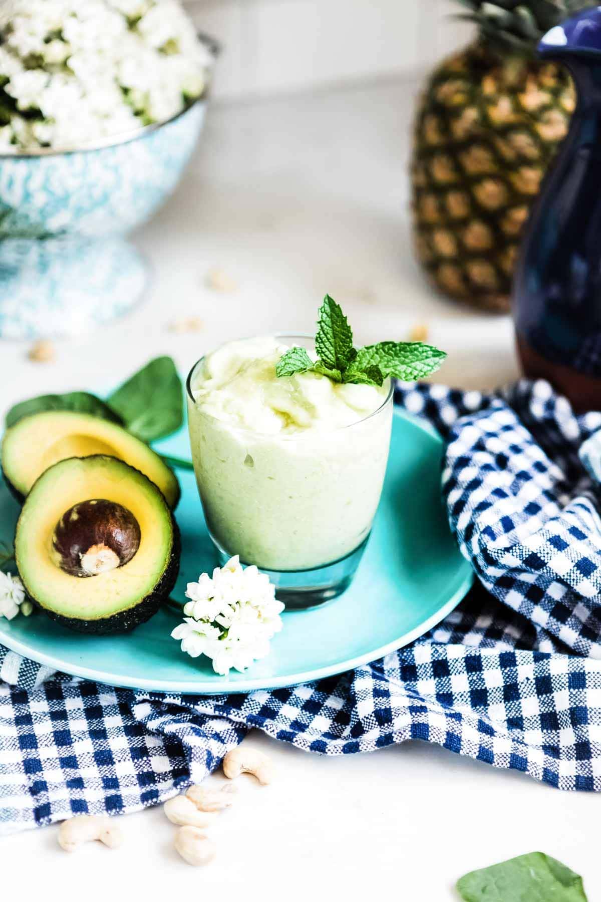 Fresh ingredients surround a glass of healthy avocado smoothie recipe on a plate.