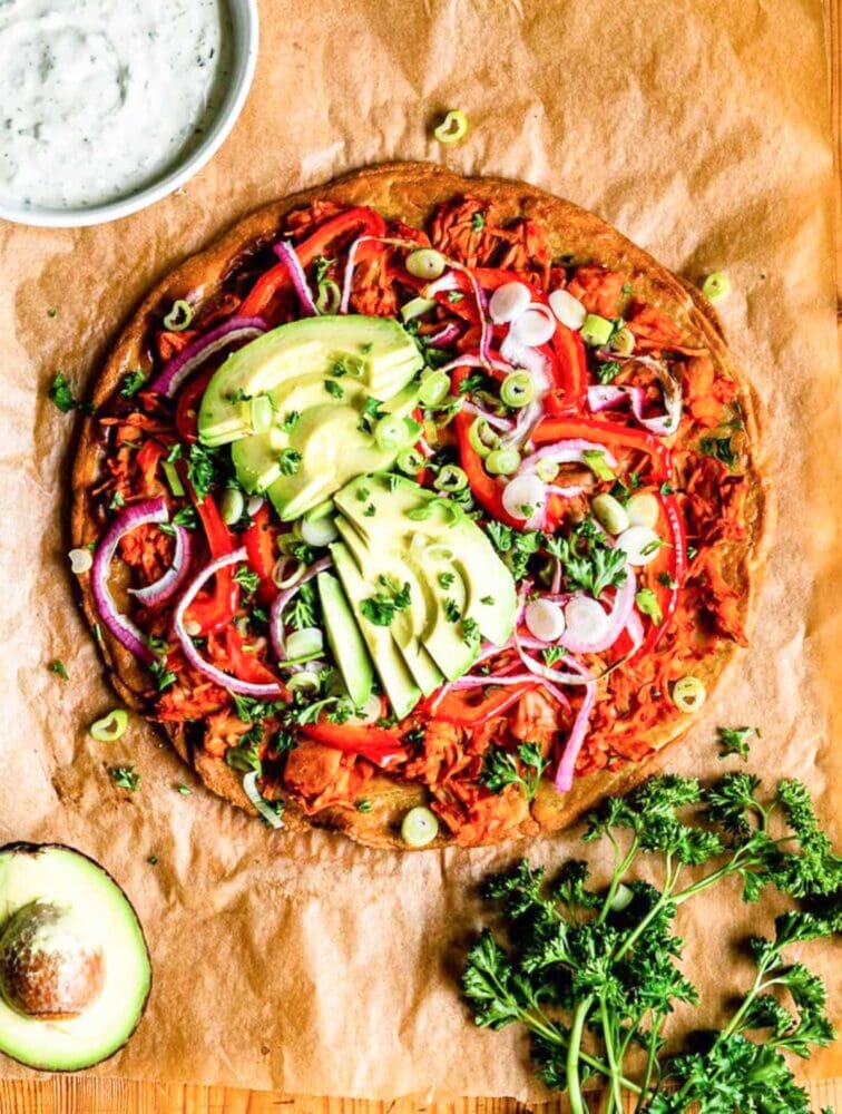 buffalo jackfruit pizza using a gluten-free pizza crust on parchment paper.