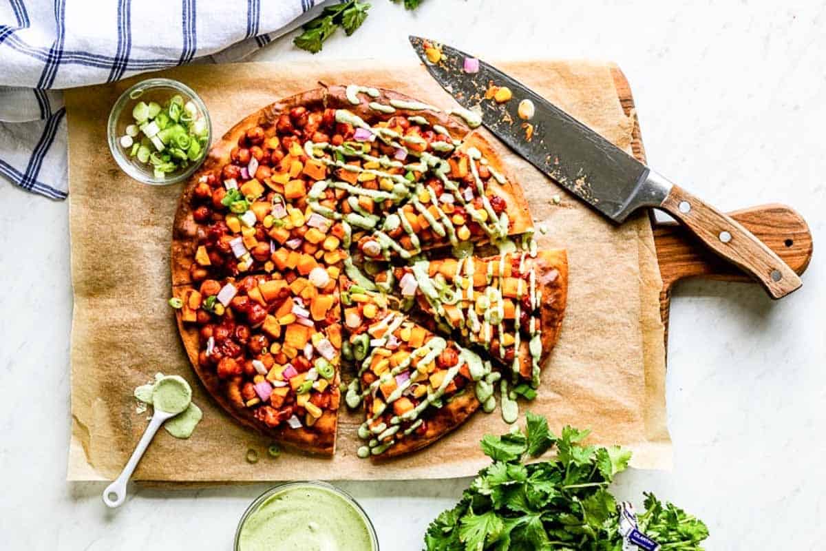 bbq vegetarian pizza sliced with a large knife on a wooden board.