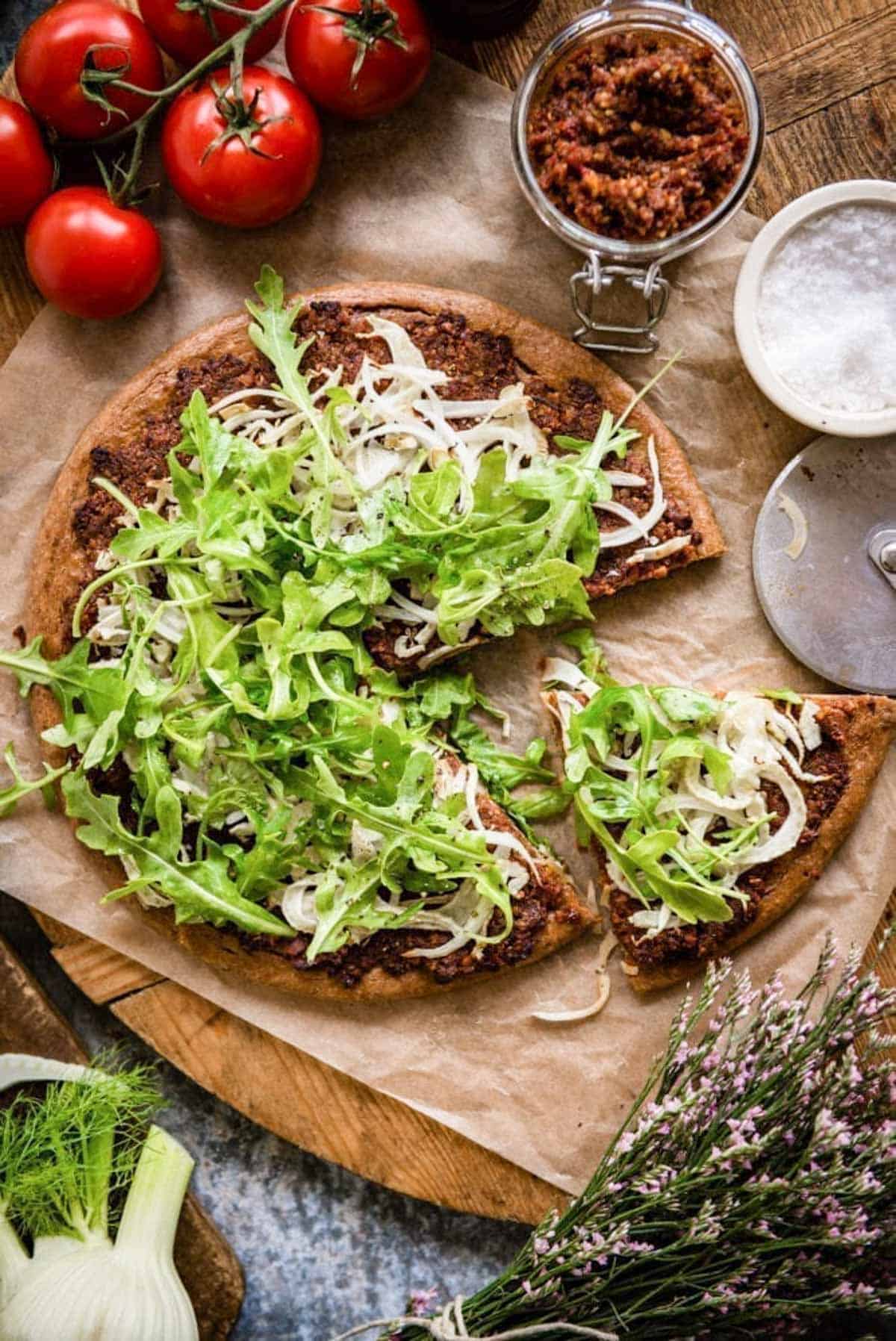 loaded pizza using a gluten-free crust and topped with sun-dried tomato pesto, arugula and fennel.