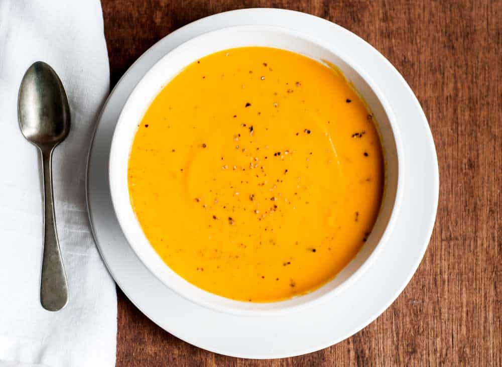 simple overhead shot of carrot soup sprinkled with cracked black pepper and loaded with delicious health benefits. 