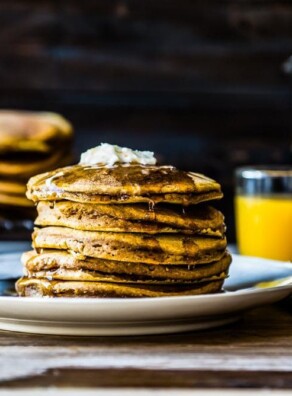 Stack of pumpkin pancakes with orange juice and coffee in the background.