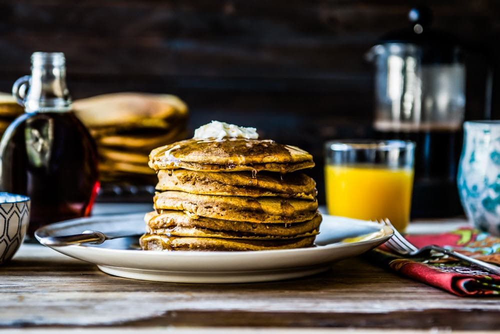 a stack of vegan pumpkin pancakes smothered in maple syrup