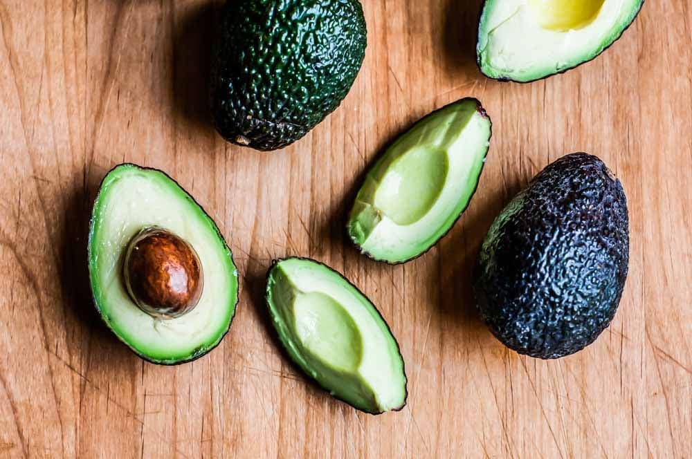 sliced and whole avocados on a wooden cutting board.