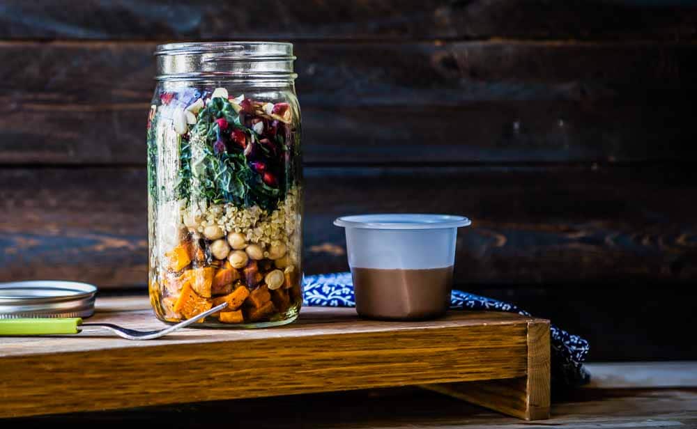 a fully layered mason jar salad with a homemade dressing next to it, ready to go