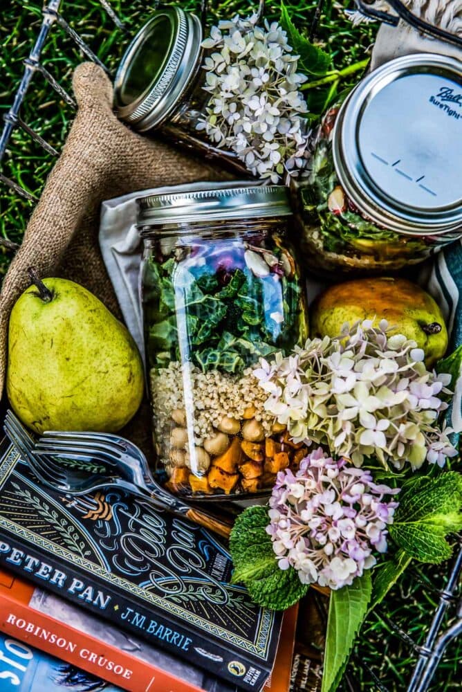 picnic basket of layered mason jar salad recipe complete with butternut squash, quinoa, kale, pomegranate, and sliced almonds.