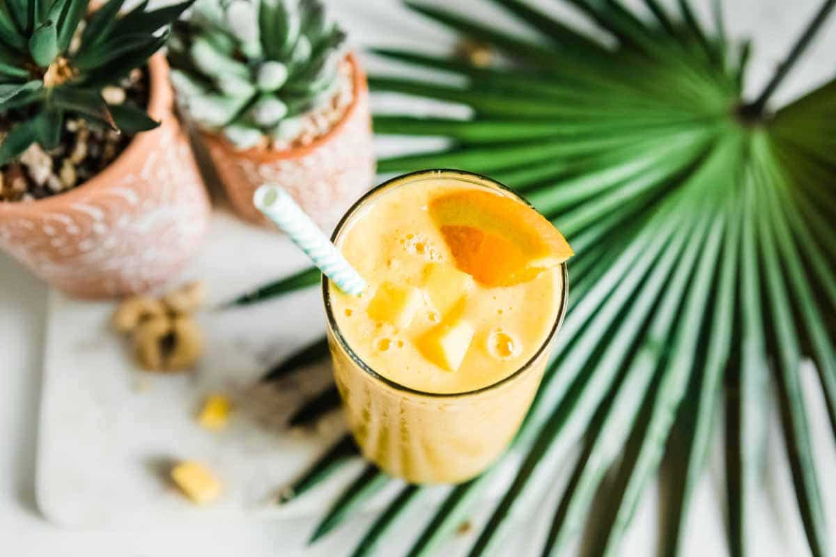 a tropical mango smoothie in a glass with a paper straw.