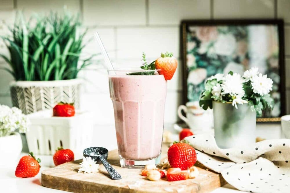 strawberry smoothie in a glass with a glass straw and a strawberry garnish.