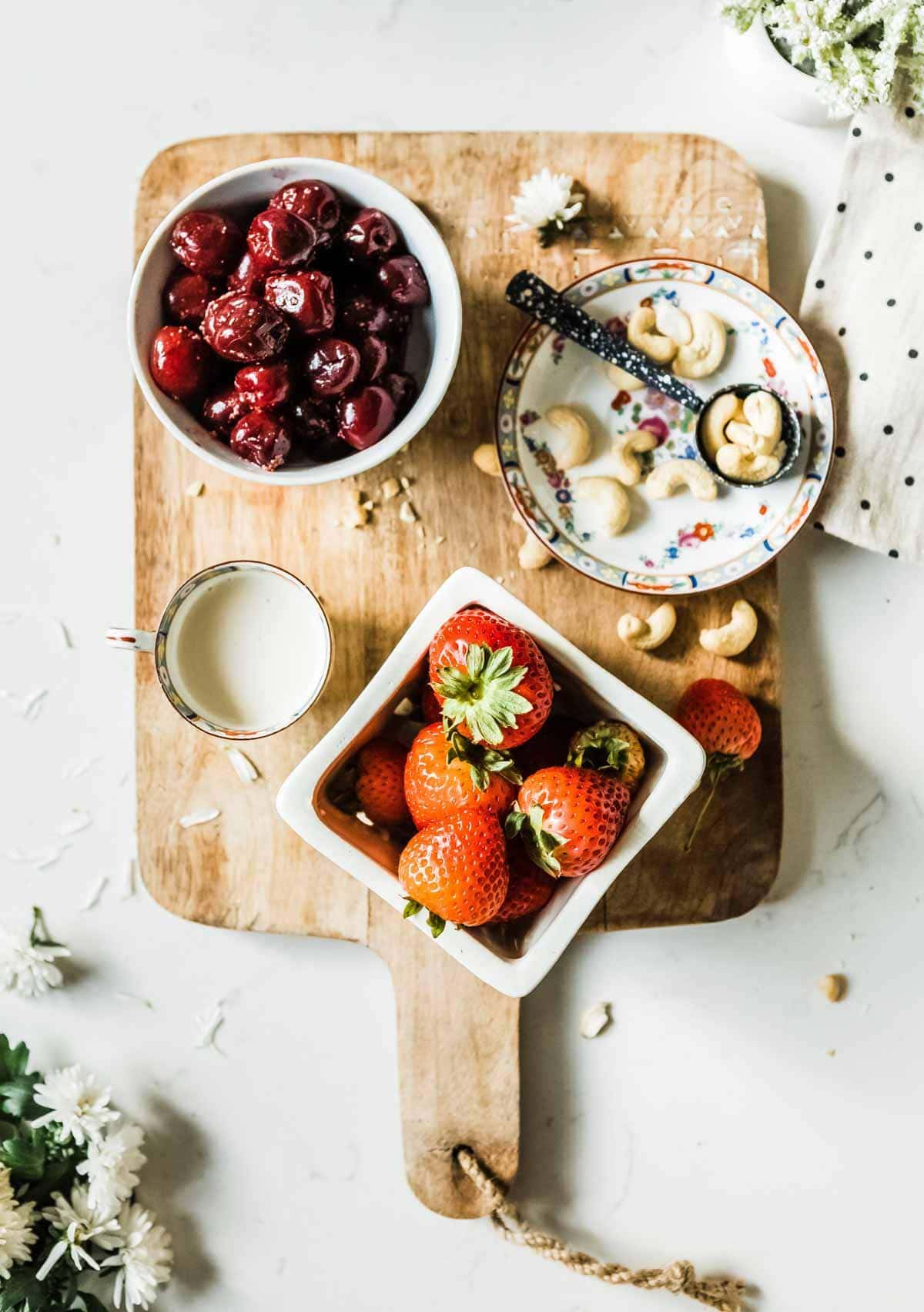 ingredients for a fruit smoothie including cherries, cashews, strawberries and cashew milk.