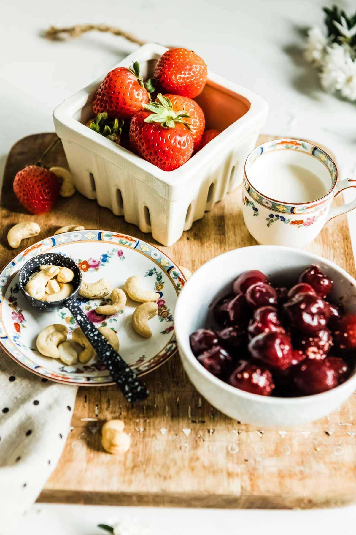 fruit smoothie ingredients including strawberries, cashews, cashew milk and cherries.