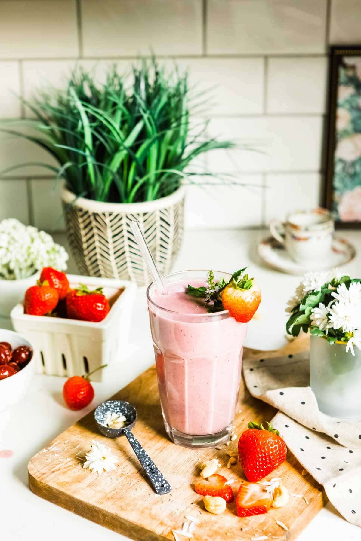 strawberry smoothie in a glass with a glass straw and a strawberry garnish.