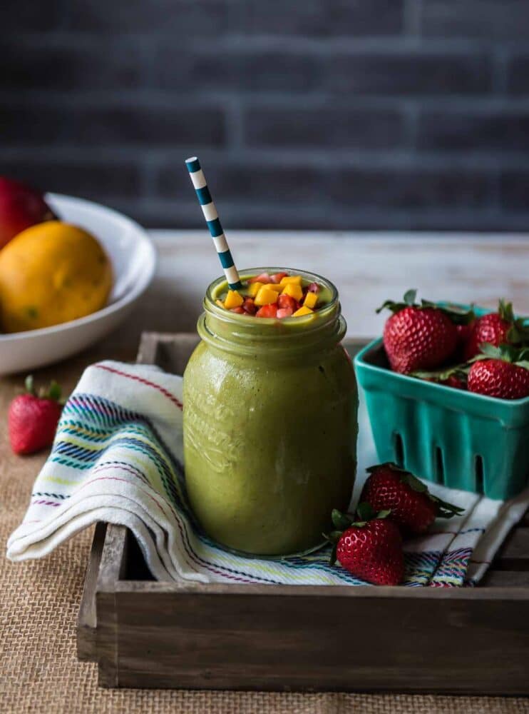 green smoothie in a glass jar sitting on a striped tea towel next to a container of fresh strawberries.