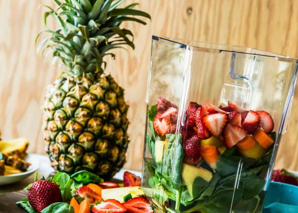 whole pineapple next to a blender container full of smoothie ingredients.