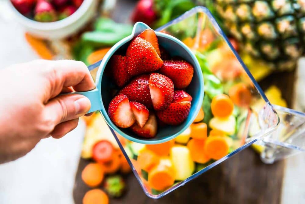 fresh strawberries in a measuring cup ready to be poured into a blender container for a carrot smoothie.