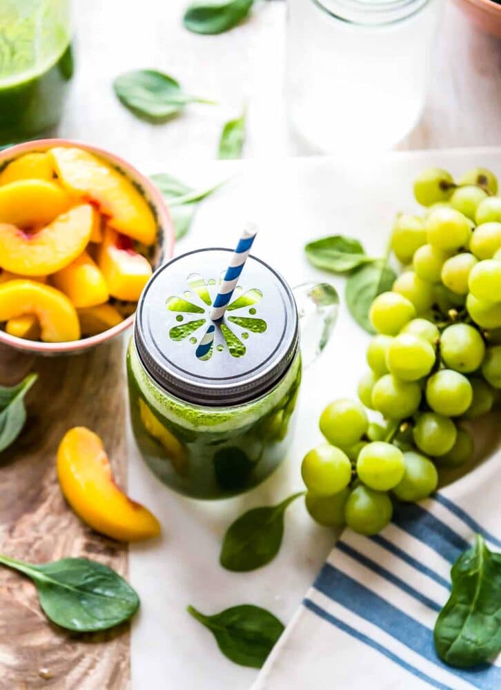 green smoothie in a glass jar with a daisy cut lid and a paper straw.